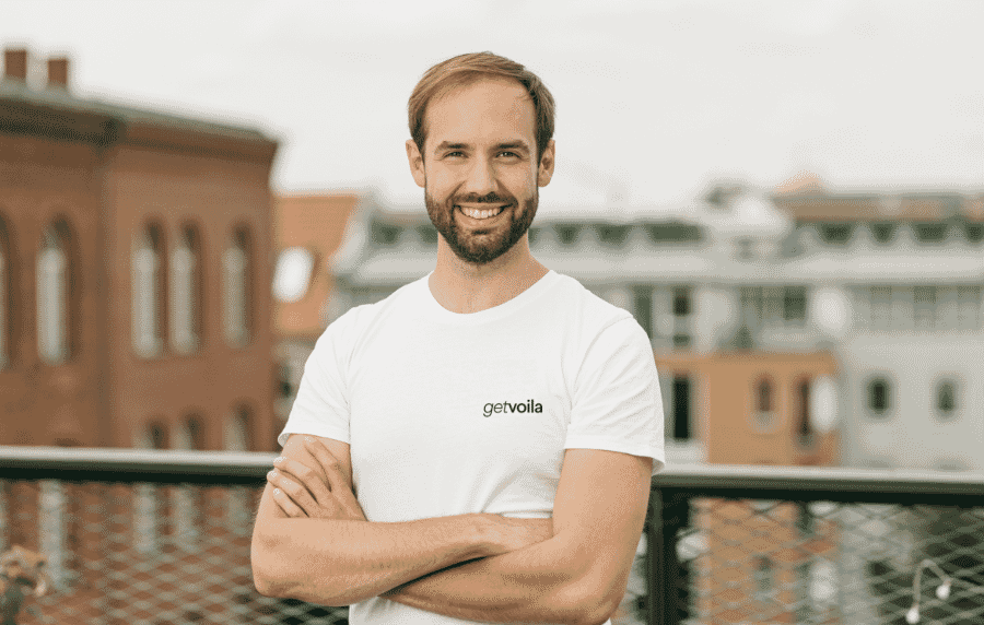 Ein lächelnder Mann in einem weißen T-Shirt steht auf einem Balkon und erhält ein Startup-Coaching.