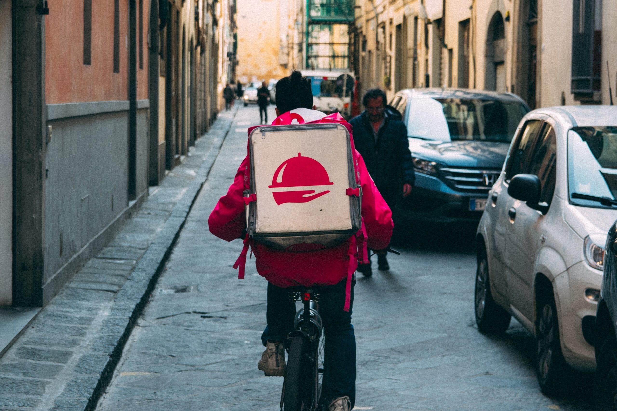 Eine Person, die mit einem Pizzakarton auf dem Rücken Fahrrad fährt, möglicherweise ein Startup-Lieferdienst.