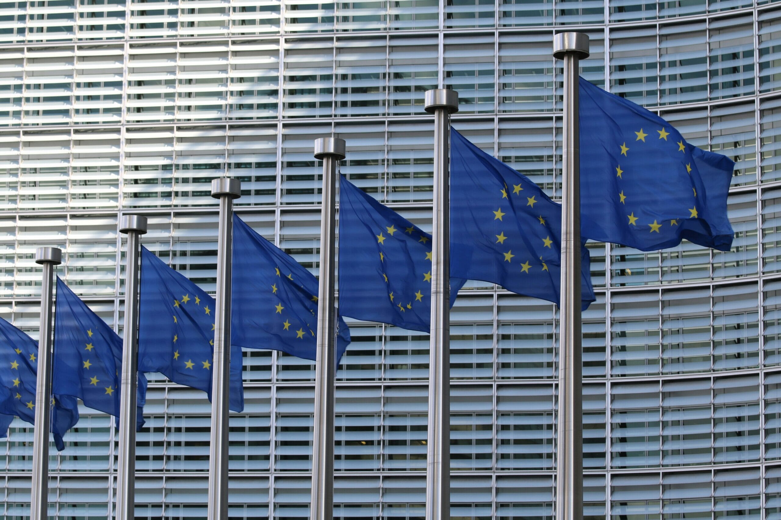Flaggen der Europäischen Union wehen vor dem Gebäude des EU-Parlaments mit horizontalen Jalousien.